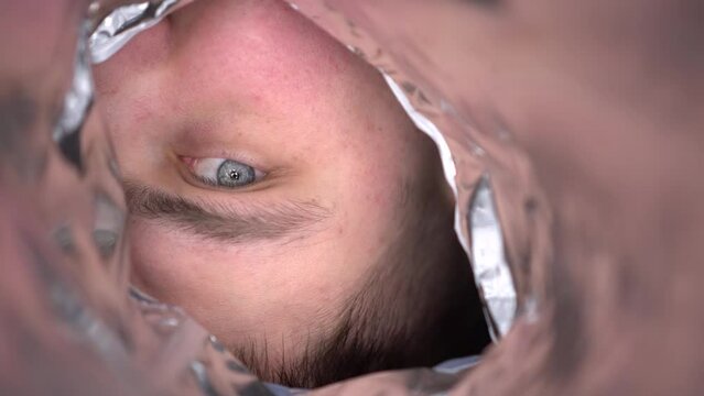 A young man looks suspiciously into an empty bag of chips. First-person view of the man's face from the package.