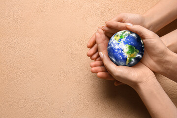 Hands of people holding small planet Earth on beige background
