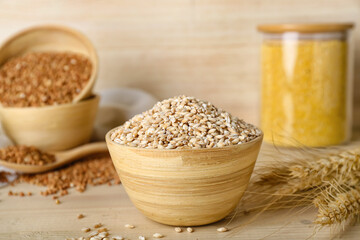 Bowl with pearl barley and spikelets on wooden background