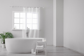 Fototapeta na wymiar Modern bathtub, houseplant and table with candles in bathroom interior