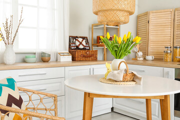 Vase with tulips, basket of Easter eggs and rabbit on dining table in kitchen