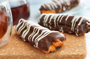 Board with delicious chocolate eclairs on white table
