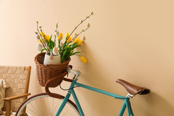 Bicycle with tree branches, Easter eggs and tulips near beige wall