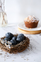 Nest with dark blue eggs for Easter and willow branches on a light background