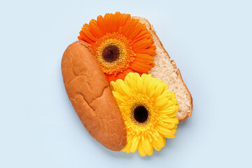 Hot dog bun with beautiful gerbera flowers on light background