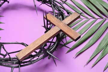 Crown of thorns with wooden cross and palm leaf on lilac background, closeup. Good Friday concept