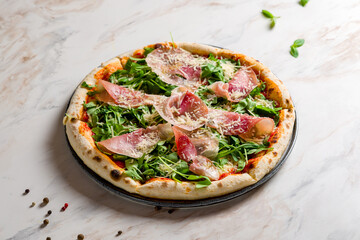 Pizza with Parma ham and arugula on white marble table