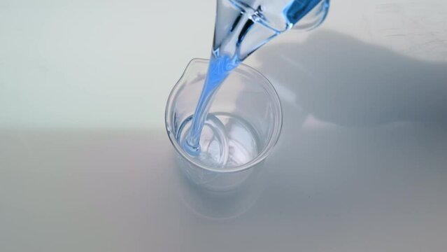 Abstract cosmetics ingredients formulating concept | Extreme close-up crane shot of cyan oil is being poured into empty beaker on grey background