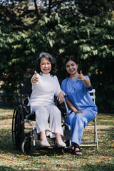 Asian young caregiver nurse support senior older male walking outdoors. Specialist girl doctor help and take care of elderly mature man patient doing physical therapy in public park at nursing home.