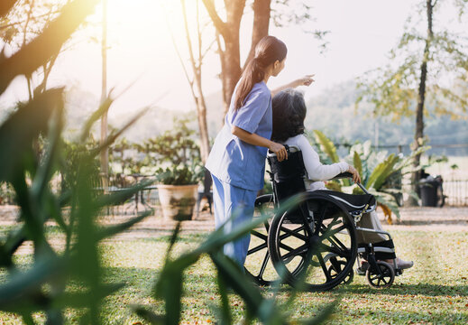 Asian Young Caregiver Nurse Support Senior Older Male Walking Outdoors. Specialist Girl Doctor Help And Take Care Of Elderly Mature Man Patient Doing Physical Therapy In Public Park At Nursing Home.