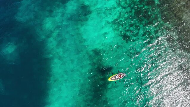 Young people couple relaxing lying floating inflatable in kayak on turquoise Adriatic Sea waves. Aerial coastal top view shot. Exotic countries vacations concept.