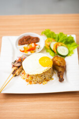 Indonesian fried rice served with a side of drumstick and satay, topped with sunny side egg