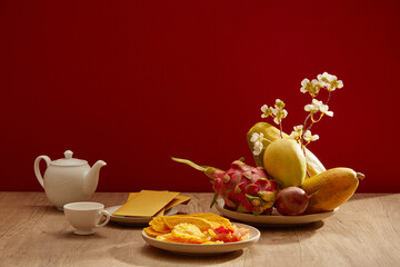 A dish of fruits with yellow envelopes, teapot, dried candies with the red-themed background....