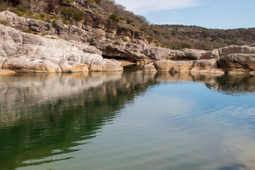 Fototapeta na wymiar A limestone rock wall creates a small canyon for the pool of green water below in Pedernales Falls State Park as part of the Texas Hill Country