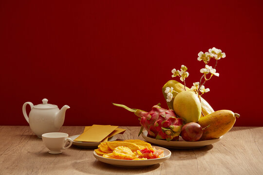 A dish of fruits with yellow envelopes, teapot, dried candies with the red-themed background. Chinese holiday concept.