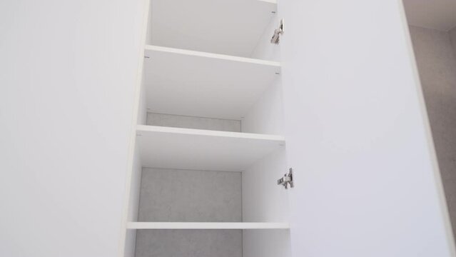 Stylish large white cabinet from floor to ceiling. Open doors in the closet, shelves. Furniture in the living room, bedroom

