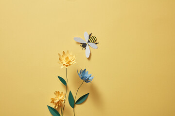 Flowers with many colors and a paper bee on light yellow background. Empty area for product or...