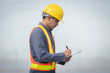 Portrait of Asian electrician engineer in safety helmet and uniform using laptop checking solar panels. Male technician at solar station.