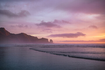Purple skies and gentle waves at Piha Beach, New Zealand.
