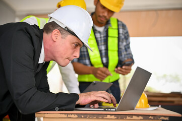 Caucasian businessman using a laptop while working with a team of construction engineers