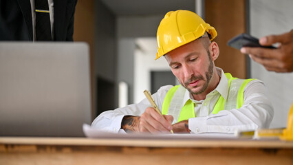 Professional Caucasian male construction engineer is drawing the building's scale on a blueprint.