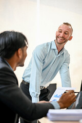 Fototapeta premium Happy caucasian male boss enjoys talking with his Asian male coworker during the meeting.