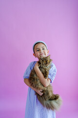 Pretty elementary girl holds fluffy brown cat in front of purple backdrop