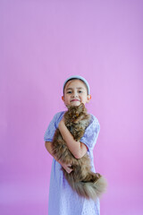 Pretty elementary girl holds fluffy brown cat in front of purple backdrop