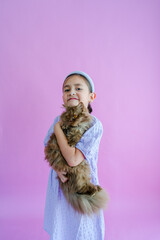 Pretty elementary girl holds fluffy brown cat in front of purple backdrop