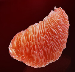 A slice of red grapefruit on a dark red background. Macro.
