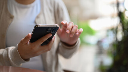 Cropped image of an Asian female relaxing in the city park and using her smartphone.