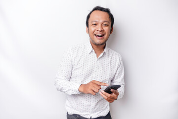 Excited Asian man wearing white shirt smiling while holding his phone, isolated by white background