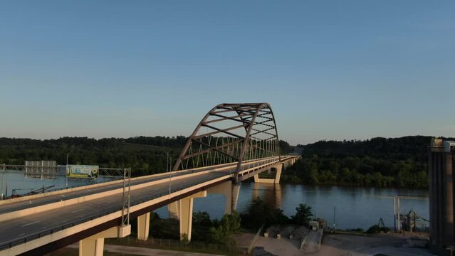 Aerial flying towards West Virginia highway bridge over Ohio river at sunset next to coal plant