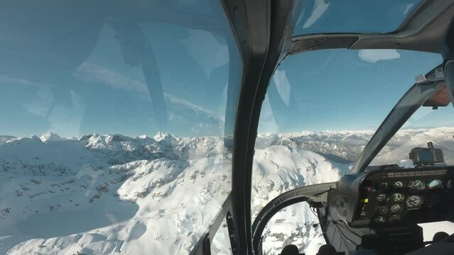 Photographer in the front seat of a helicopter ride, flying through the snowy mountains of Canada, BC