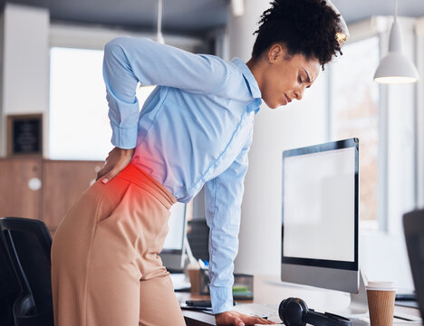 Back pain, office and business black woman with injury, muscle ache and spine problem standing at desk. Medical emergency, stress and tired female worker massage body for strain, tension and accident
