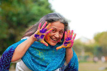 Indian senior woman playing colors and celebrating holi festival.