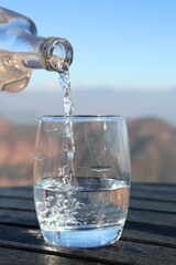 clean and fresh spring drinking Water pouring from the bottle into a glass on a wooden table outdoors. Snow clad Himalayas mountains in the background. Pure Himalayan spring water. copy space.