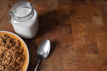 Cereal in the yellow bowl and glass of milk on butcher block surface