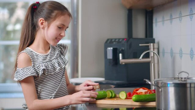 Preteen girl cut vegetables for salad in kitchen. Realtime