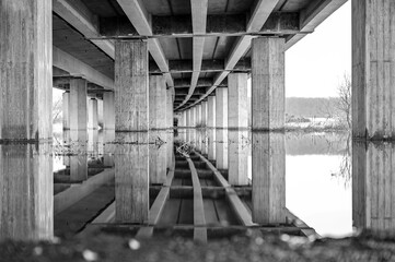 Reflection under a highway bridge with bridge pillars in the water of the flood in black and white