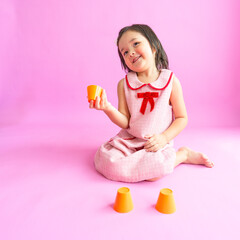 Pretty little girls sitting on floor and playing with three orange cups. She is trying to find the prize under one cup. 