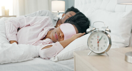 Black woman waking up in bed to switch off her alarm clock with a sleep mask in her house. Lazy,...
