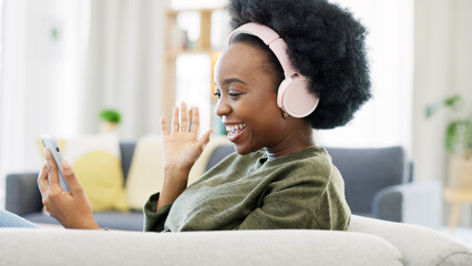 Cheerful african afro woman using phone and headphones and waving while on a video call with...