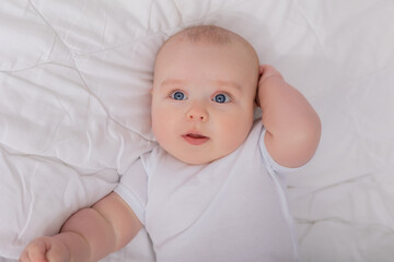 blue-eyed baby in a white bodysuit lies in a crib and looks at the camera