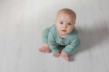 portrait of a charming chubby baby in a green jumpsuit sitting on the floor. top view
