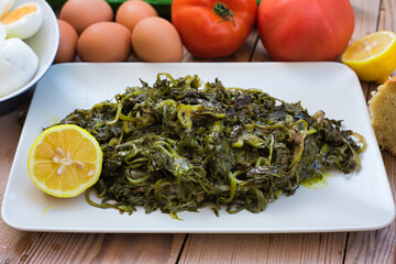 salad with boiled wild greens, dandelion, lemons and extra virgin olive oil, on a wooden table.  Horta or Wild Greens. Greek Cuisine.