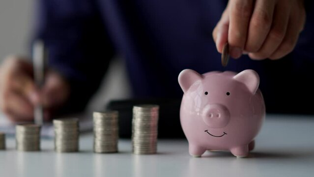 Businessman hands puts a coin in a pink piggy bank. The concept of saving money or savings.