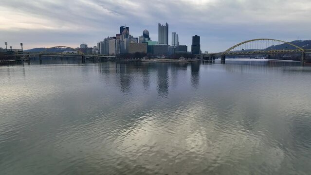 Aerial glide over Ohio River with Pittsburgh skyline, Point State Park, and yellow bridges in background.