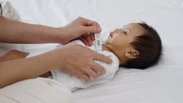 mother measuring temperature at armpit of newborn baby on a bed