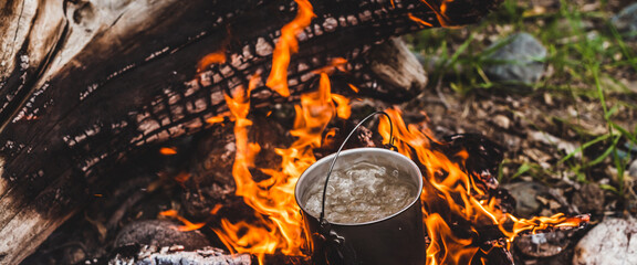 Kettle stands on fire. Cooking food at fire in wild. Beautiful big log burns in bonfire close-up....